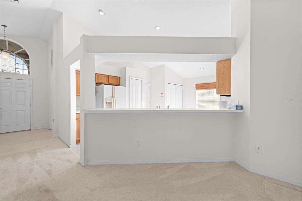 A view of a carpeted living area looking toward a kitchen with a breakfast bar — 13233 BAINBRIDGE WAY, SPRING HILL, FL