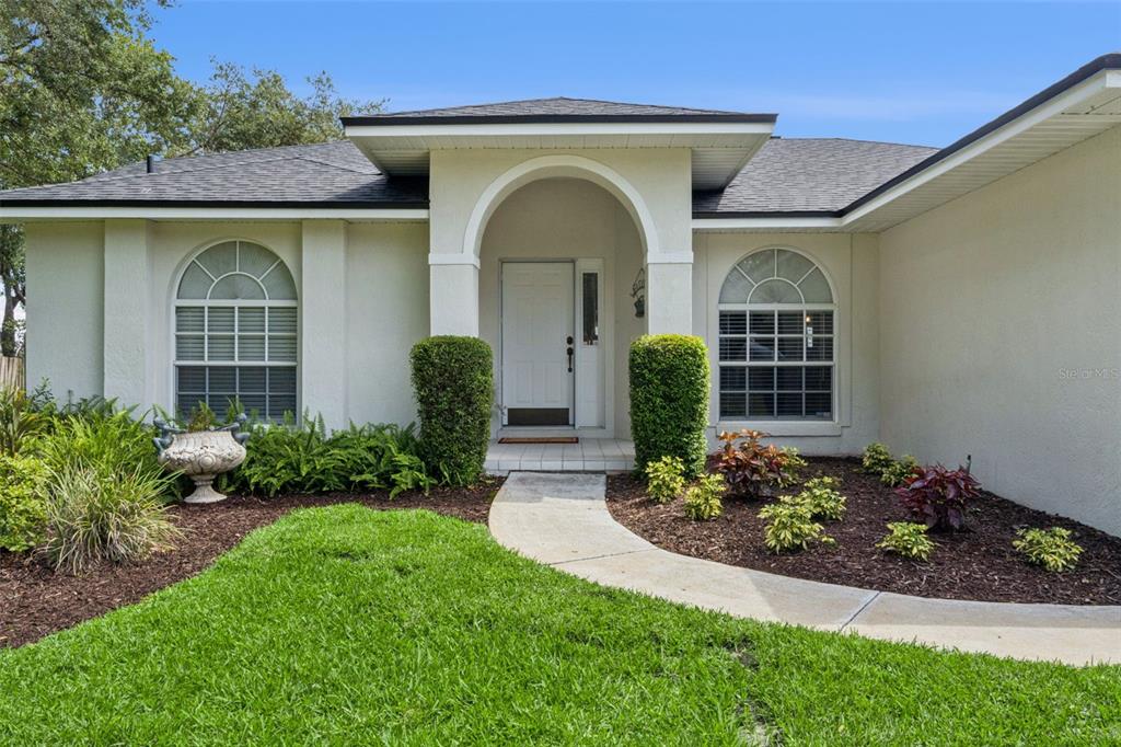 A single-story house exterior features a white arched entryway, two arched windows, and landscaped gardens — 3339 SLASH PINE DRIVE, LAKE WALES, FL