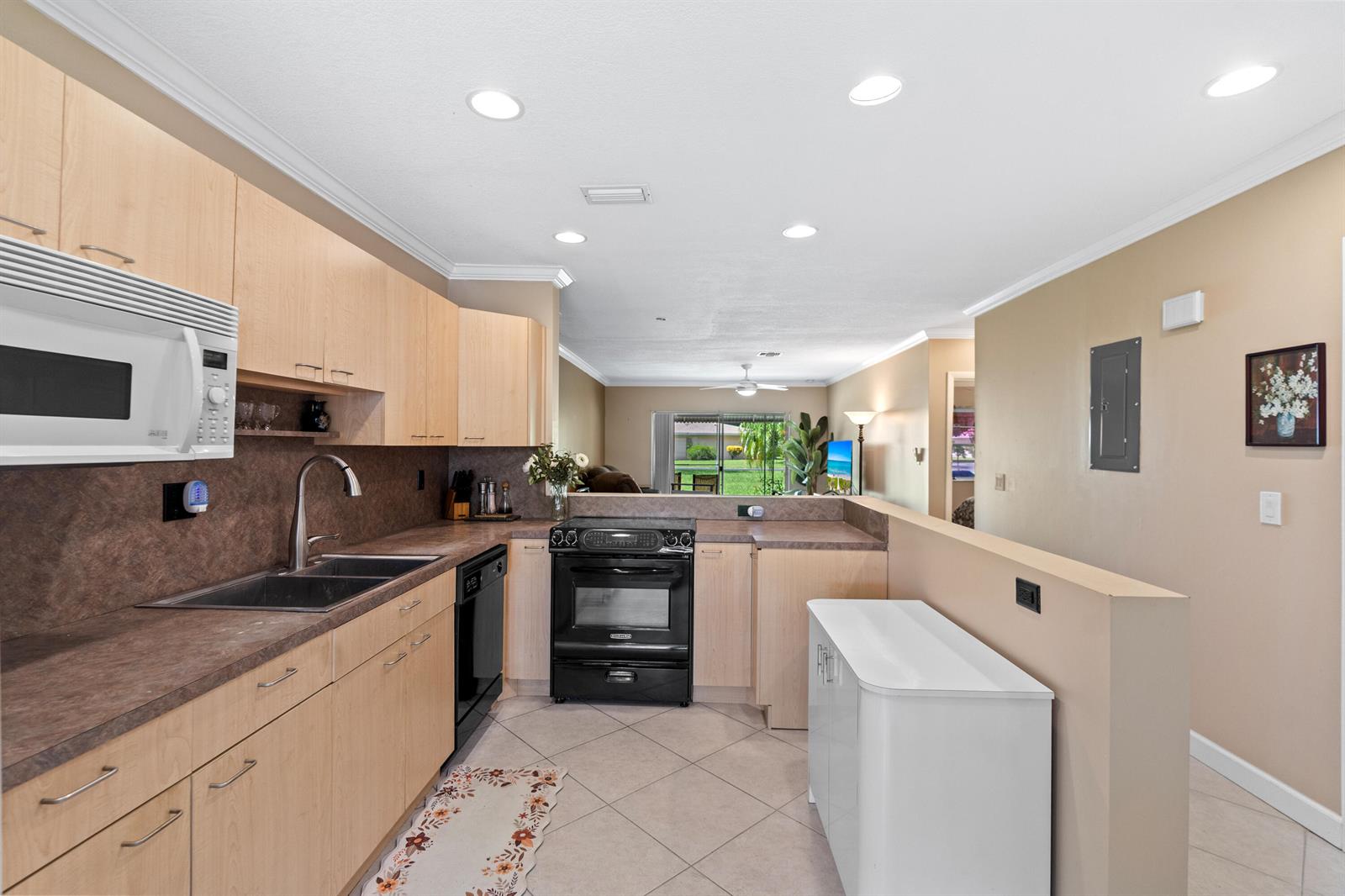 A kitchen with light wood cabinets, dark countertops, and black appliances opens to a living area — 8666 Bella Vista Drive # 111, Boca Raton FL 33433, BOCA RATON, FL