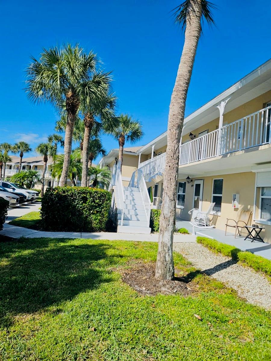Exterior view of a two-story apartment building with white stairs, balconies, and palm trees — 1335 Mainsail Dr # 1315, Naples FL 34114, NAPLES, FL