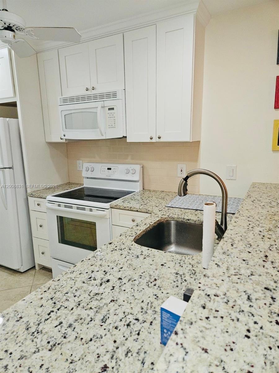 A kitchen features white cabinets, granite countertops, a stainless steel sink, and white appliances — 1335 Mainsail Dr # 1315, Naples FL 34114, NAPLES, FL
