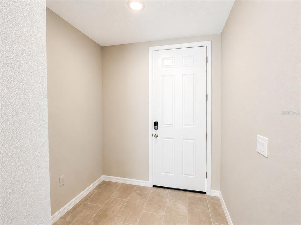 An entryway features a white six-panel door, beige walls, and light-colored tile flooring — 5909 SAILOR COAST WAY, NOKOMIS, FL