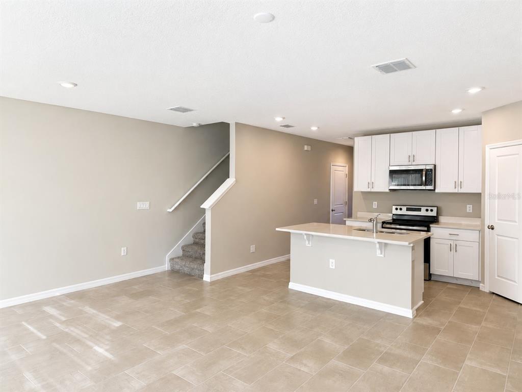 An open-concept kitchen with white cabinets and an island overlooks a living area with stairs — 5909 SAILOR COAST WAY, NOKOMIS, FL