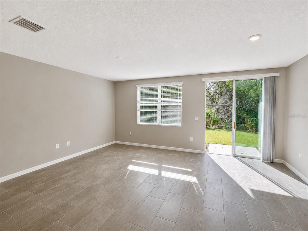 An empty room with light gray walls, tile flooring, a window, and a sliding glass door — 5909 SAILOR COAST WAY, NOKOMIS, FL