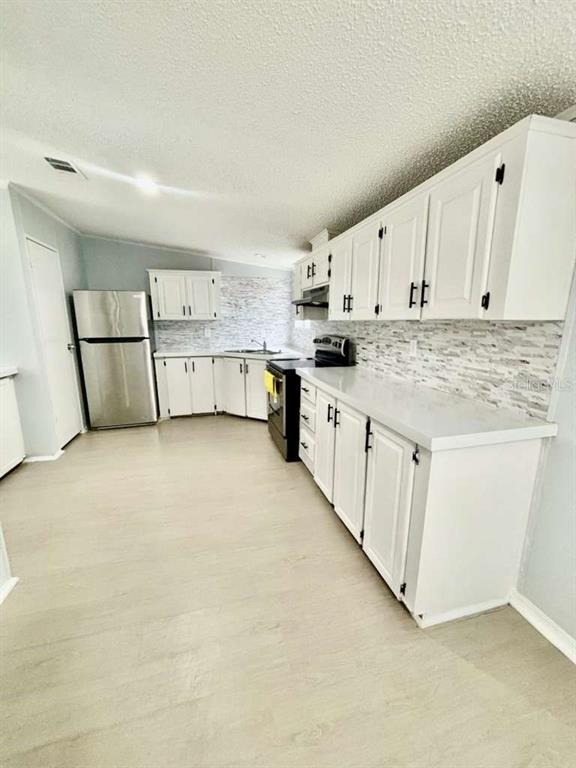 A kitchen features white cabinets, stainless steel appliances, and a light-colored tiled backsplash — 218 DIAMOND ACRES ROAD, DAVENPORT, FL