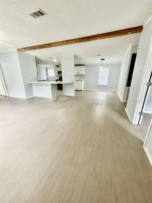 An open-concept living area features light wood-look flooring, white walls, and a wooden ceiling beam — 218 DIAMOND ACRES ROAD, DAVENPORT, FL