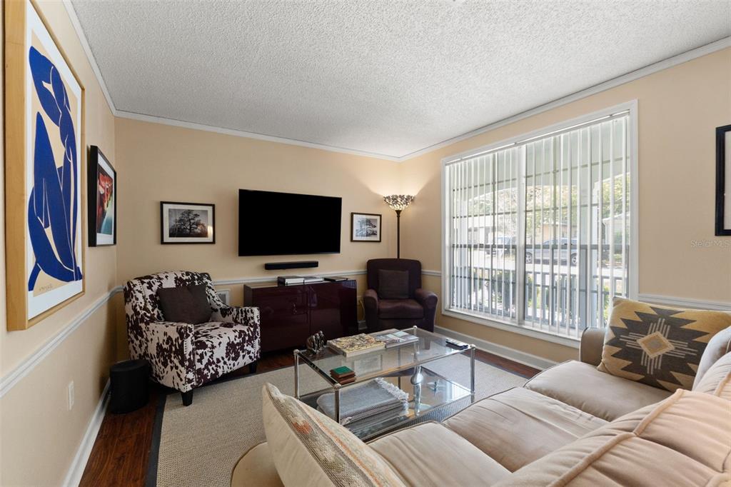 A living room features a beige sofa, patterned armchair, glass coffee table, and wall-mounted television — 8802 SEELEY LANE, HUDSON, FL