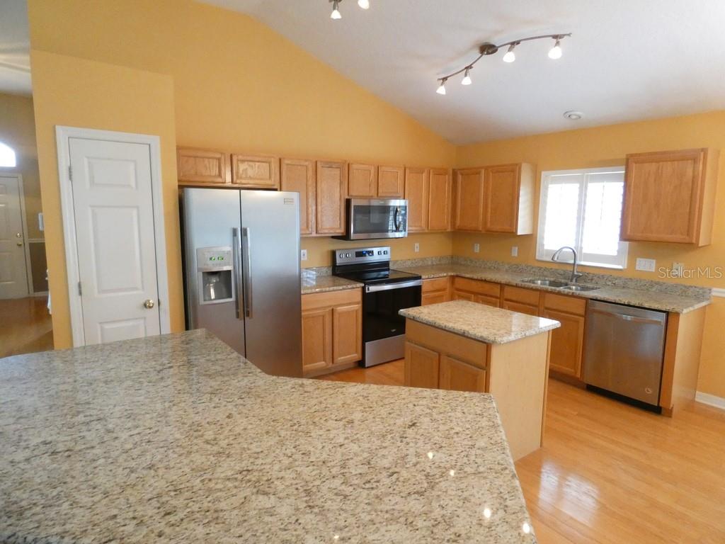 A kitchen features light wood cabinets, granite countertops, stainless steel appliances, and a center island — 6200 ASHFIELD PLACE, WESLEY CHAPEL, FL
