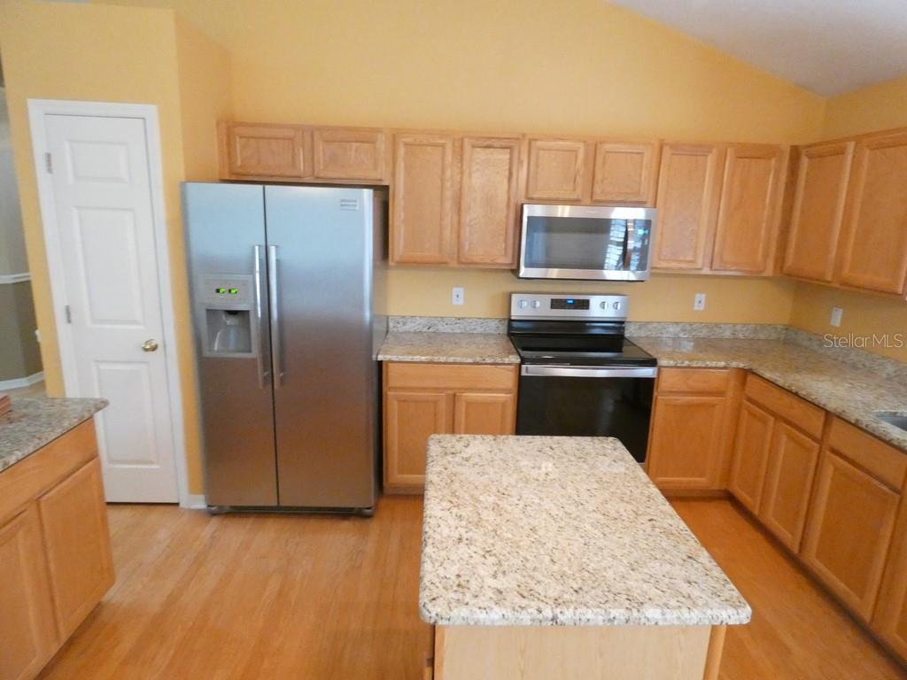 A kitchen features light wood cabinets, granite countertops, stainless steel appliances, and a central island — 6200 ASHFIELD PLACE, WESLEY CHAPEL, FL