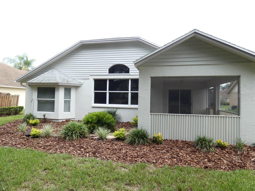 The exterior of a house features a screened-in porch, a bay window, and landscaped mulch — 6200 ASHFIELD PLACE, WESLEY CHAPEL, FL
