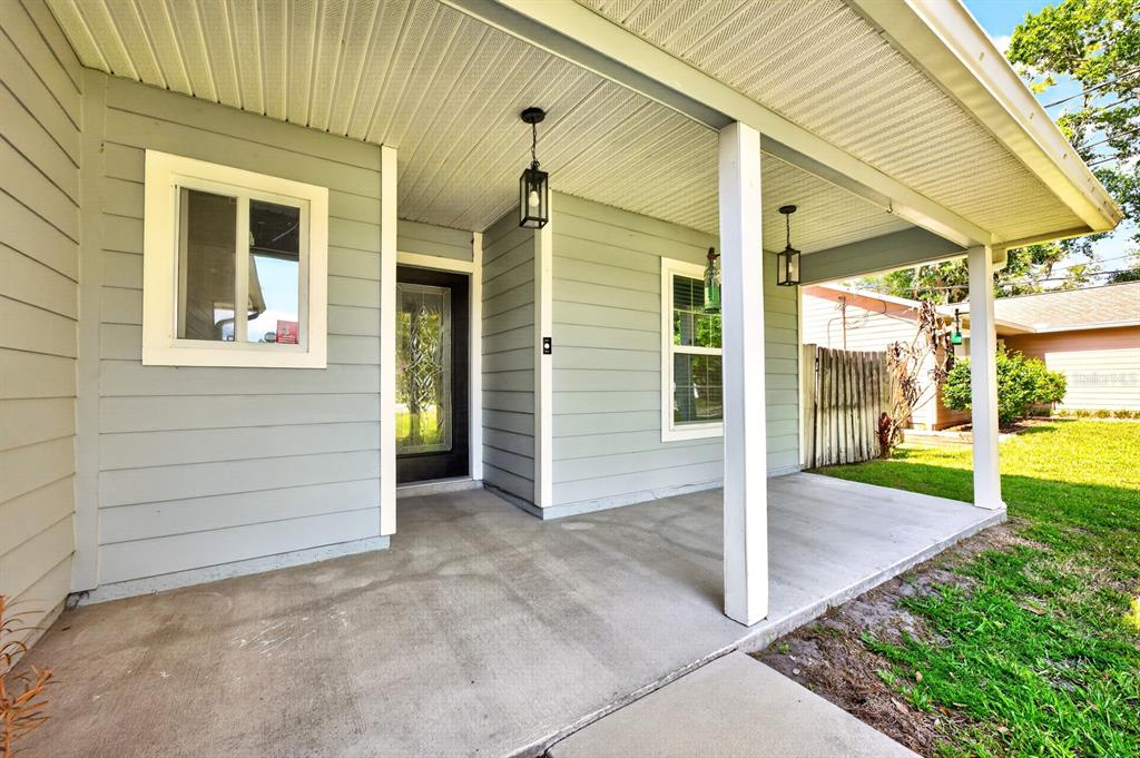 A covered concrete front porch with light gray siding, two hanging lanterns, and a front door — 116 W 5TH STREET, CHULUOTA, FL