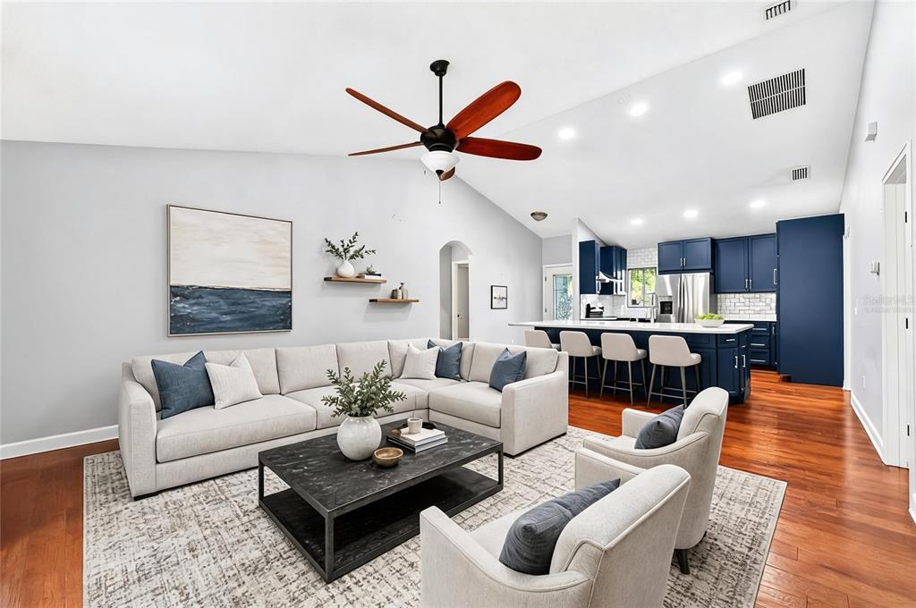 A living room with a sectional sofa, two armchairs, and an open kitchen with blue cabinets — 116 W 5TH STREET, CHULUOTA, FL