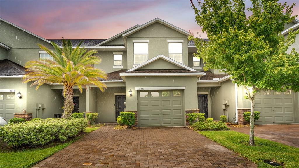 A multi-unit residential building features a brick driveway, a palm tree, and attached garages — 6441 TORRINGTON CIRCLE, LAKELAND, FL
