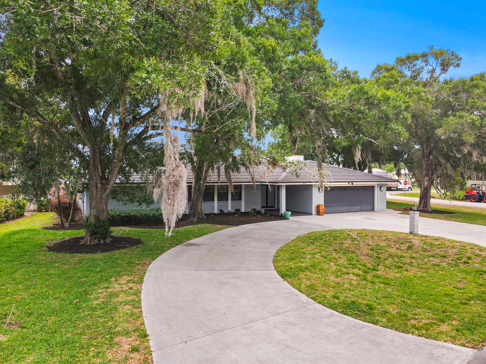 A single-story gray brick house features a curved concrete driveway and large oak trees — 7312 Elyse Circle, Port St. Lucie FL 34952, PORT ST. LUCIE, FL