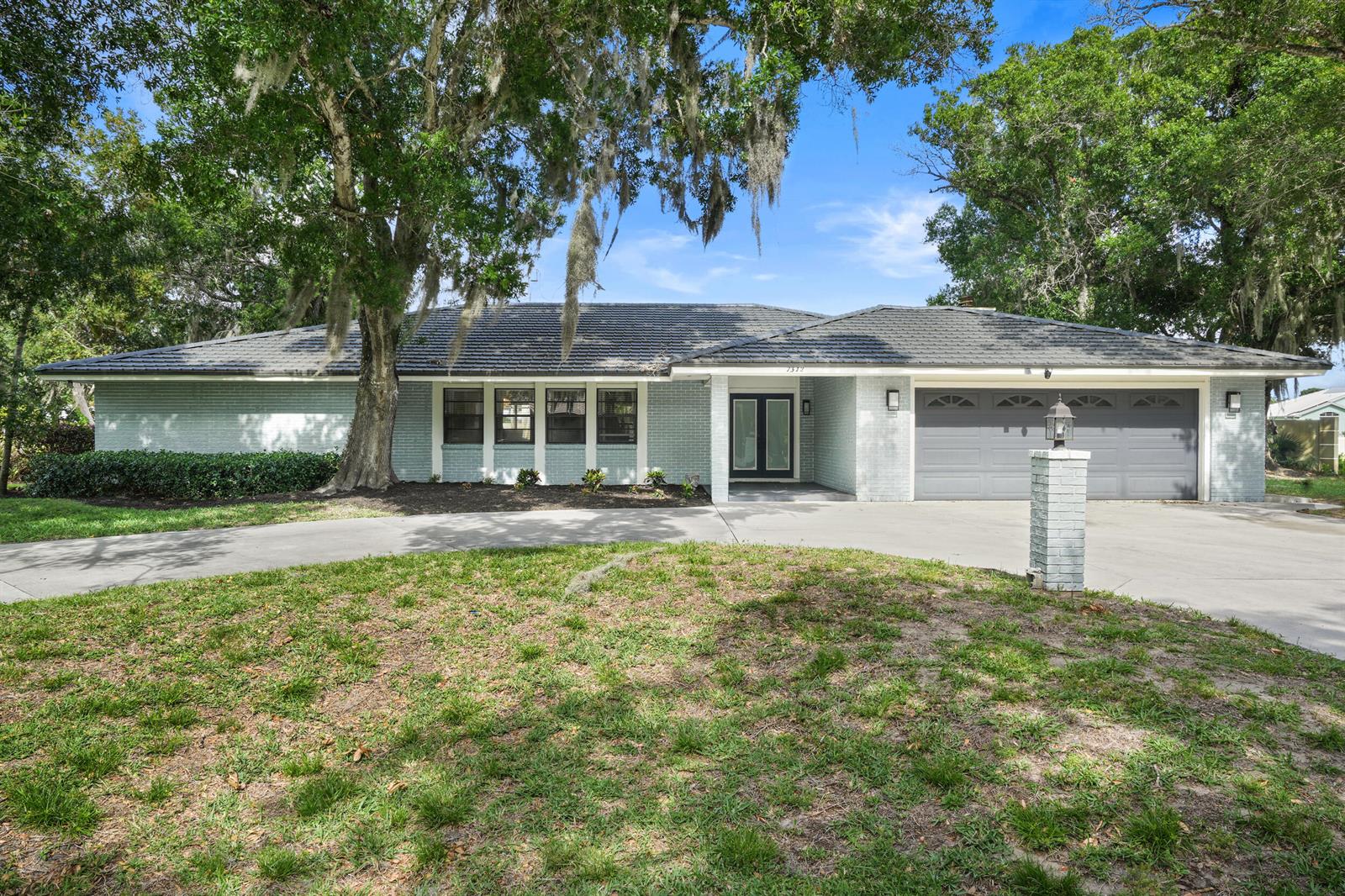 A single-story house with a light-colored brick exterior, dark roof, and a two-car garage — 7312 Elyse Circle, Port St. Lucie FL 34952, PORT ST. LUCIE, FL
