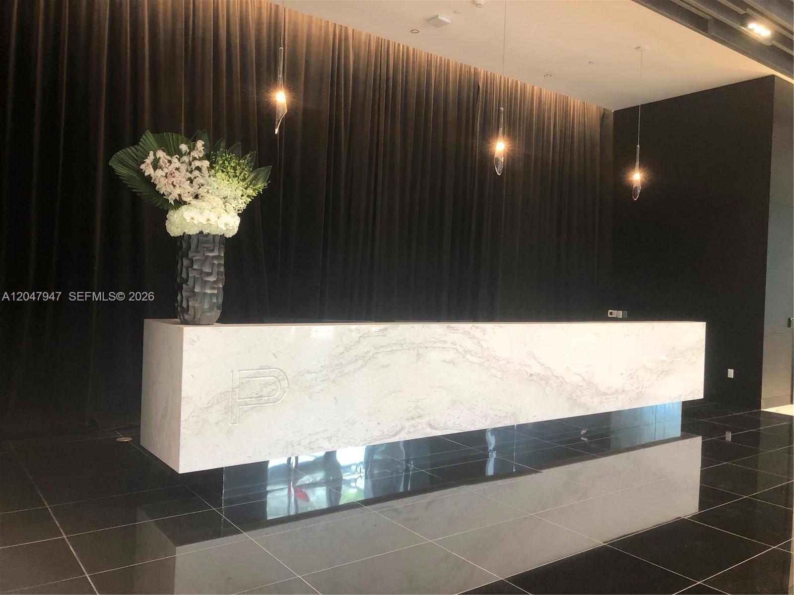 A modern reception area features a marble desk with a logo, dark curtains, and pendant lighting — 851 NE 1st Ave # 3705, Miami FL 33132, MIAMI, FL