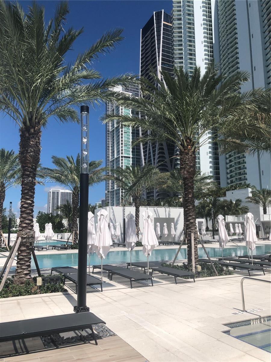 A swimming pool area features lounge chairs, white umbrellas, palm trees, and modern high-rise buildings — 851 NE 1st Ave # 3705, Miami FL 33132, MIAMI, FL