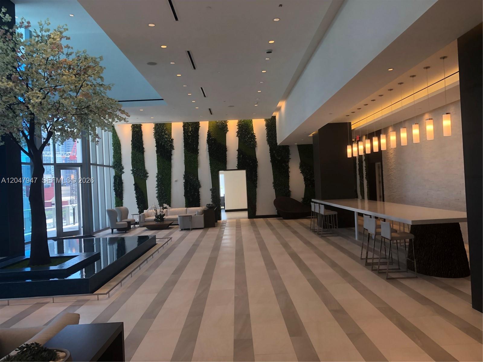 A modern lobby features a large indoor tree, a water feature, and a long bar — 851 NE 1st Ave # 3705, Miami FL 33132, MIAMI, FL
