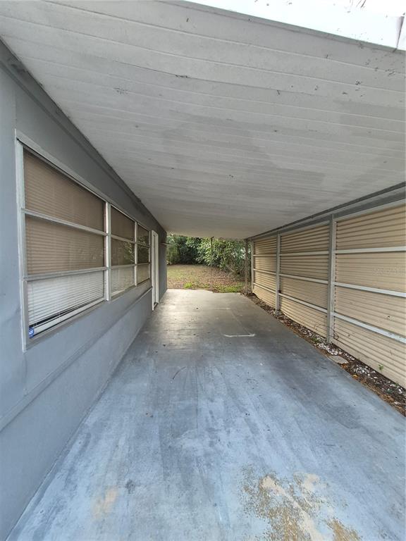 A covered concrete carport sits between a grey house wall and a tan metal fence — 11 S BARBOUR STREET, BEVERLY HILLS, FL