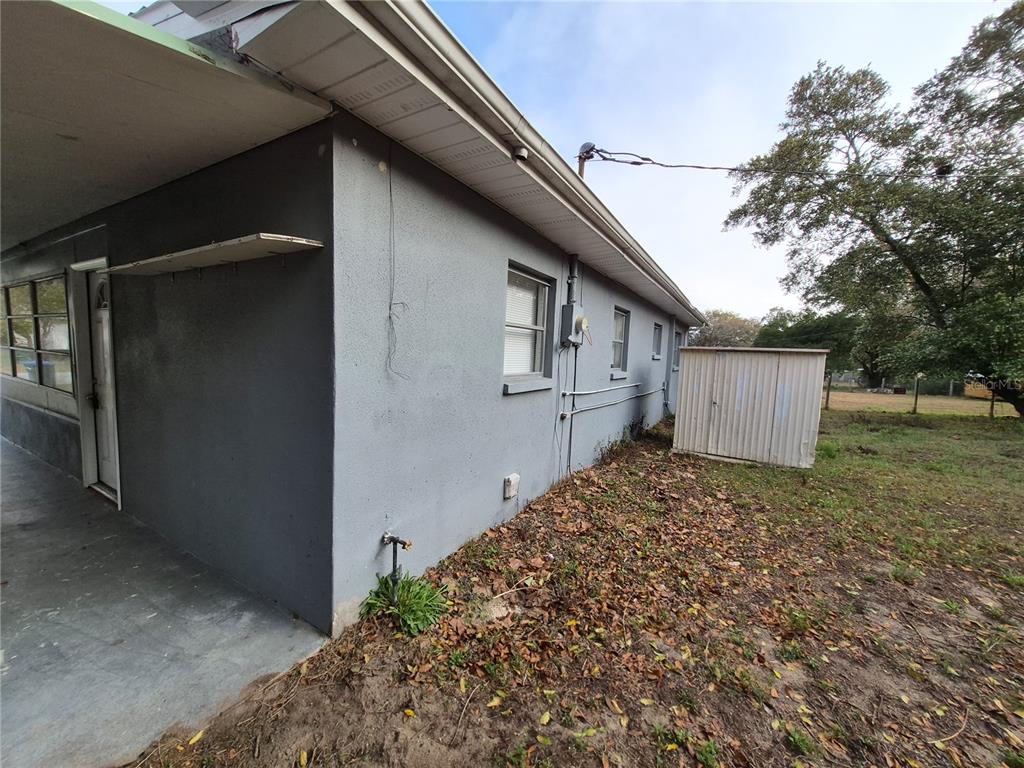 A side view of a gray stucco house with a porch and a metal shed — 11 S BARBOUR STREET, BEVERLY HILLS, FL
