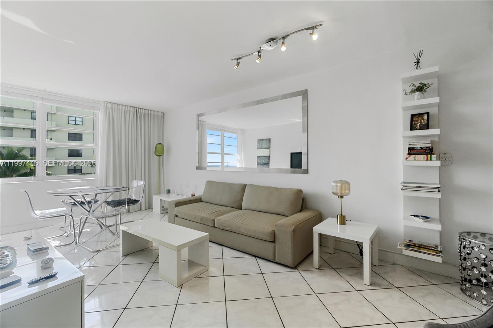 A living room features a beige sofa, white tile floors, a large mirror, and dining area — 100 Lincoln Rd # 638, Miami Beach FL 33139, MIAMI BEACH, FL