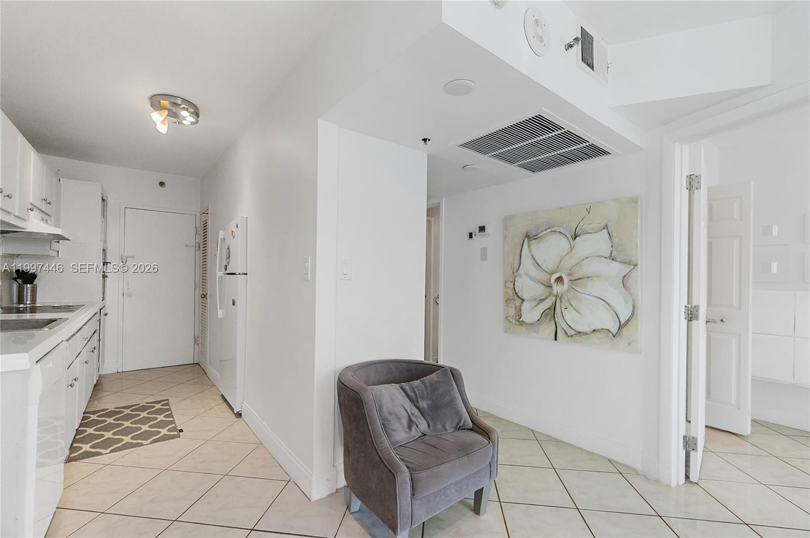 A kitchen area with white cabinets and a grey armchair in the adjacent hallway — 100 Lincoln Rd # 638, Miami Beach FL 33139, MIAMI BEACH, FL
