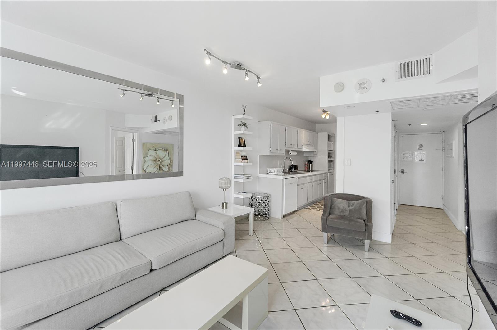A living room with a sofa, coffee table, and an open kitchen with white cabinets — 100 Lincoln Rd # 638, Miami Beach FL 33139, MIAMI BEACH, FL