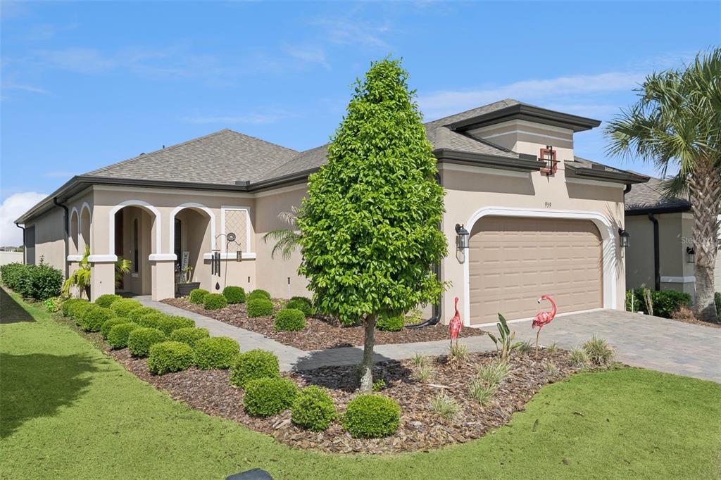 A single-story house with a tan stucco exterior, a two-car garage, and manicured landscaping — 959 BRAEWOOD DRIVE, CLERMONT, FL