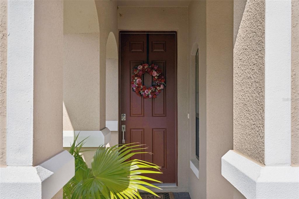 A brown front door with a floral wreath is framed by beige stucco columns — 959 BRAEWOOD DRIVE, CLERMONT, FL