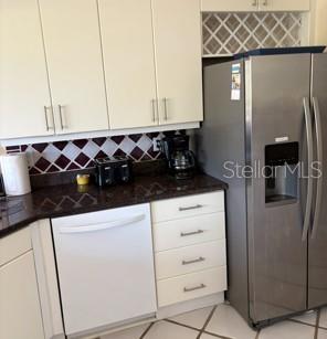 A kitchen features white cabinets, dark granite countertops, a stainless steel refrigerator, and a dishwasher — 8974 GREY OAKS AVENUE, SARASOTA, FL