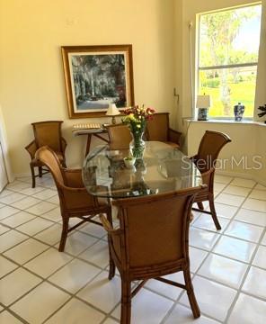 A dining room with a glass-topped table, rattan chairs, and tile flooring near a window — 8974 GREY OAKS AVENUE, SARASOTA, FL