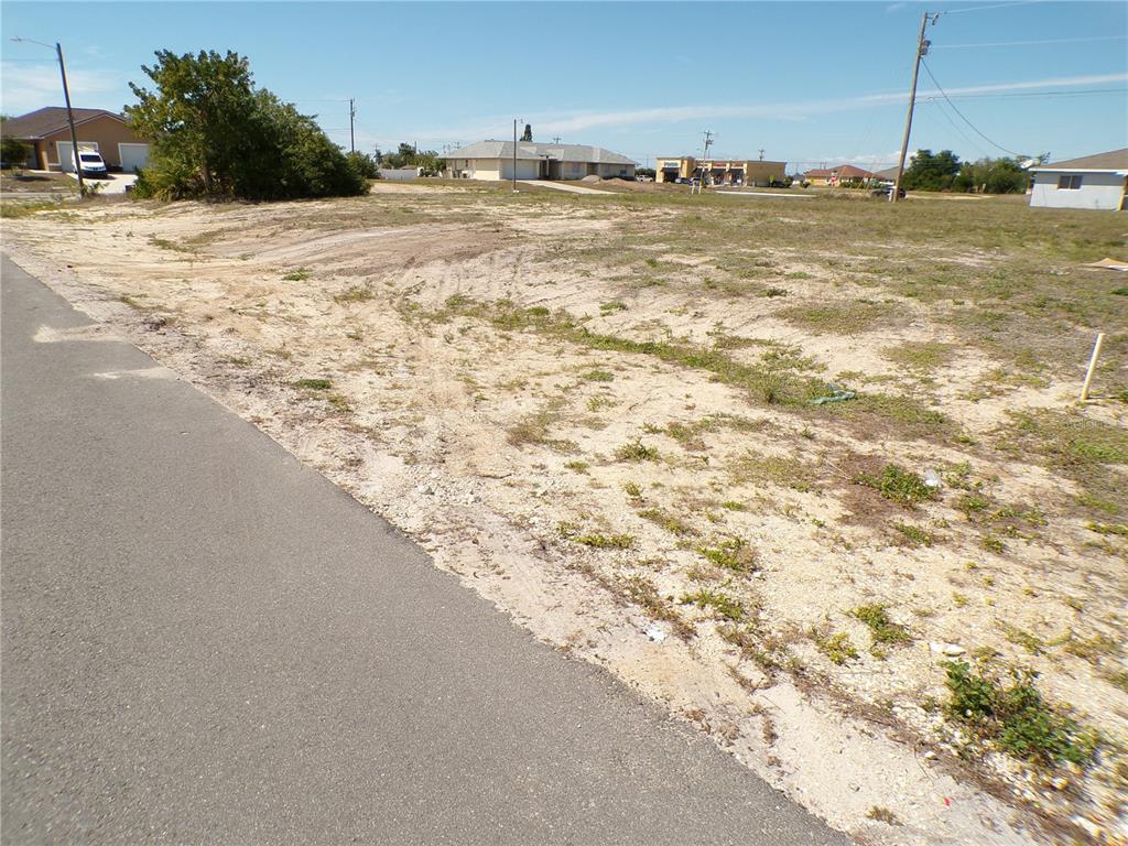 A vacant, sandy residential lot sits adjacent to a paved road under a clear sky — 825 NE 15TH LANE, CAPE CORAL, FL