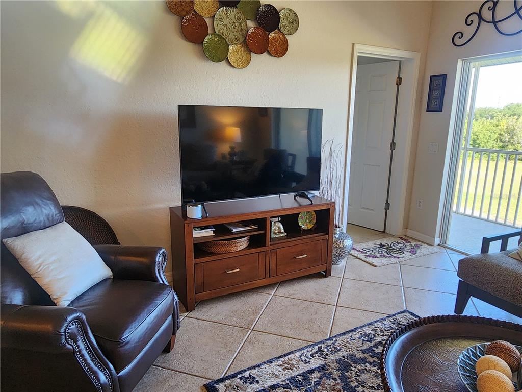 A living room features a television on a wooden stand, a leather armchair, and tile flooring — 7224 CEDAR HOLLOW CIRCLE, BRADENTON, FL