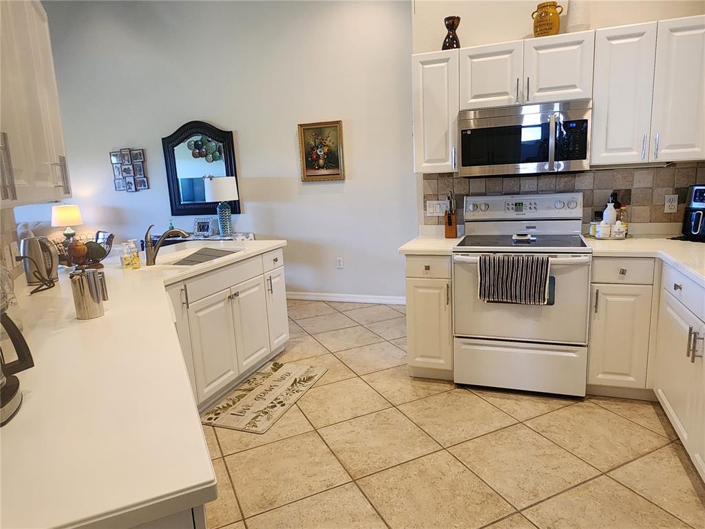 A kitchen with white cabinets, stainless steel appliances, and tile flooring opens to a living area — 7224 CEDAR HOLLOW CIRCLE, BRADENTON, FL
