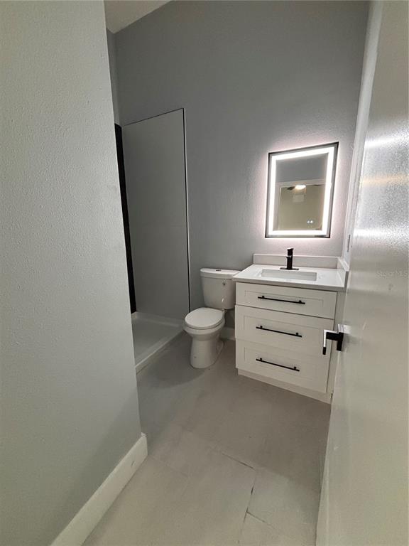 A bathroom with a white vanity, a toilet, a shower stall, and a lighted mirror — 2818 HARGILL DRIVE, ORLANDO, FL