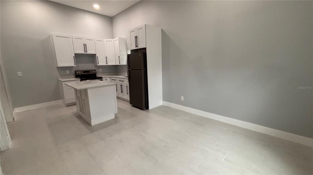 A kitchen with white cabinets, a central island, and a dark refrigerator on tiled floors — 2818 HARGILL DRIVE, ORLANDO, FL
