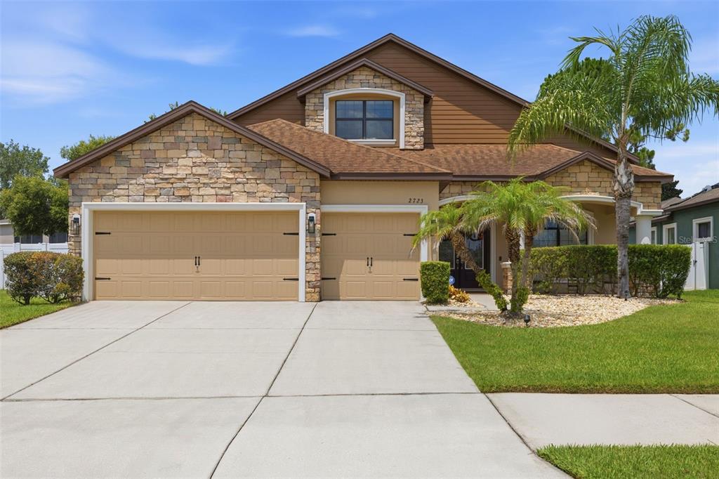 A two-story house with a stone facade, tan garage doors, and a palm tree — 2723 COLEWOOD LANE, DOVER, FL
