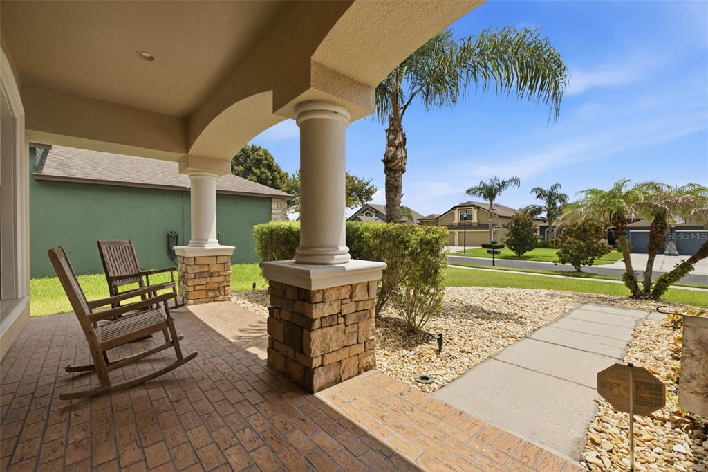 A covered front porch features two wooden rocking chairs, stone columns, and a brick floor — 2723 COLEWOOD LANE, DOVER, FL