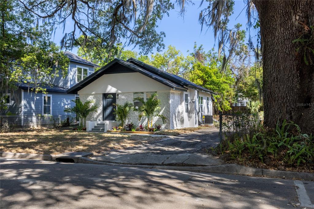 A white, single-story house with a dark roof and palm trees sits near a street — 418 NW 3RD AVENUE, GAINESVILLE, FL