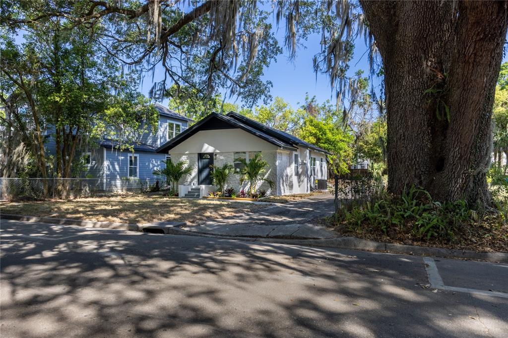 A white single-story house with a black roof sits behind a large oak tree — 418 NW 3RD AVENUE, GAINESVILLE, FL