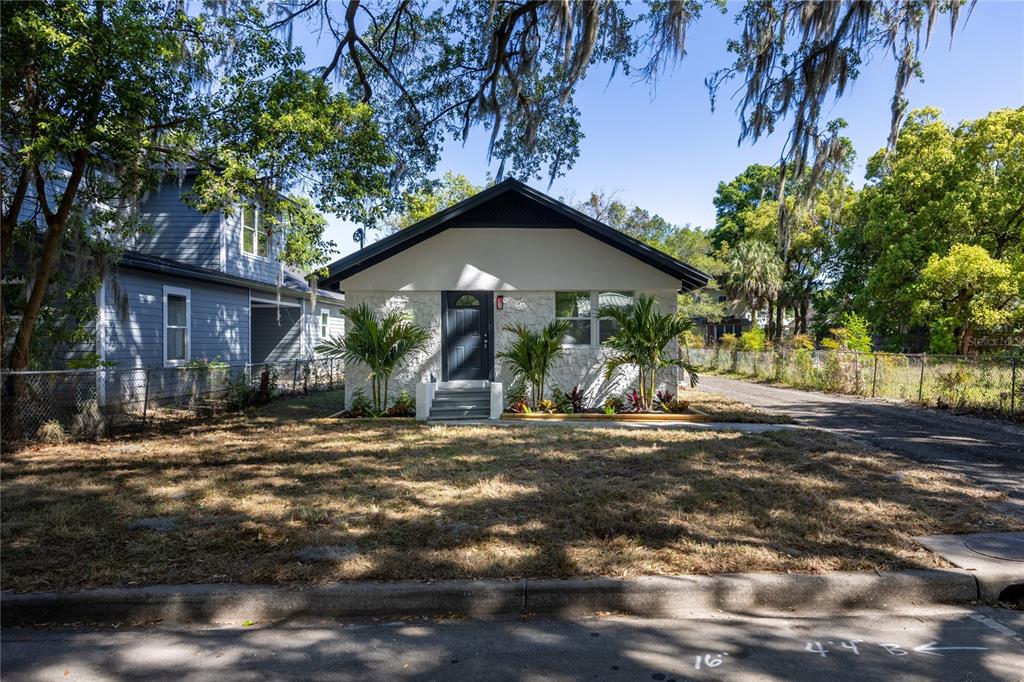 A single-story house with white stone siding and a dark roof sits behind a lawn — 418 NW 3RD AVENUE, GAINESVILLE, FL
