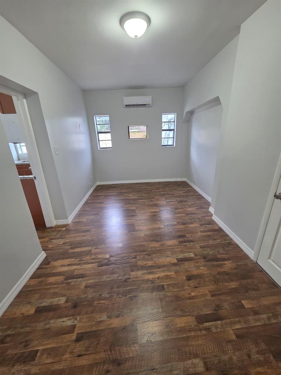 An empty room features wood-look flooring, light gray walls, two windows, and a wall-mounted air conditioner — 31 Edmund Road # 5, West Park FL 33023, WEST PARK, FL