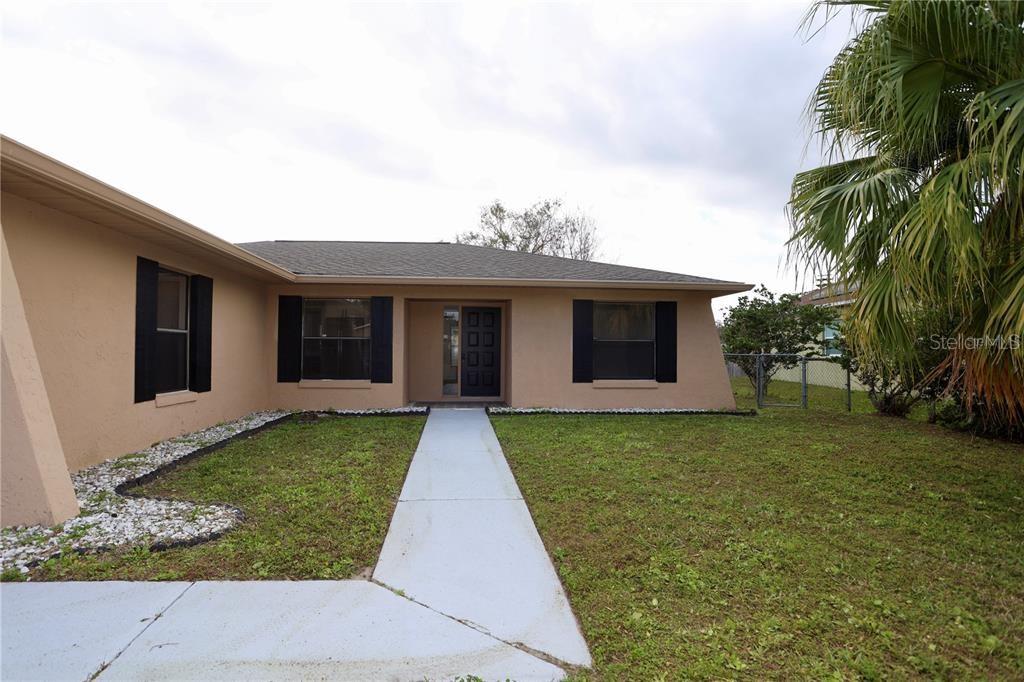 A single-story house with tan stucco walls, black shutters, and a concrete walkway — 620 HERALDO COURT, KISSIMMEE, FL