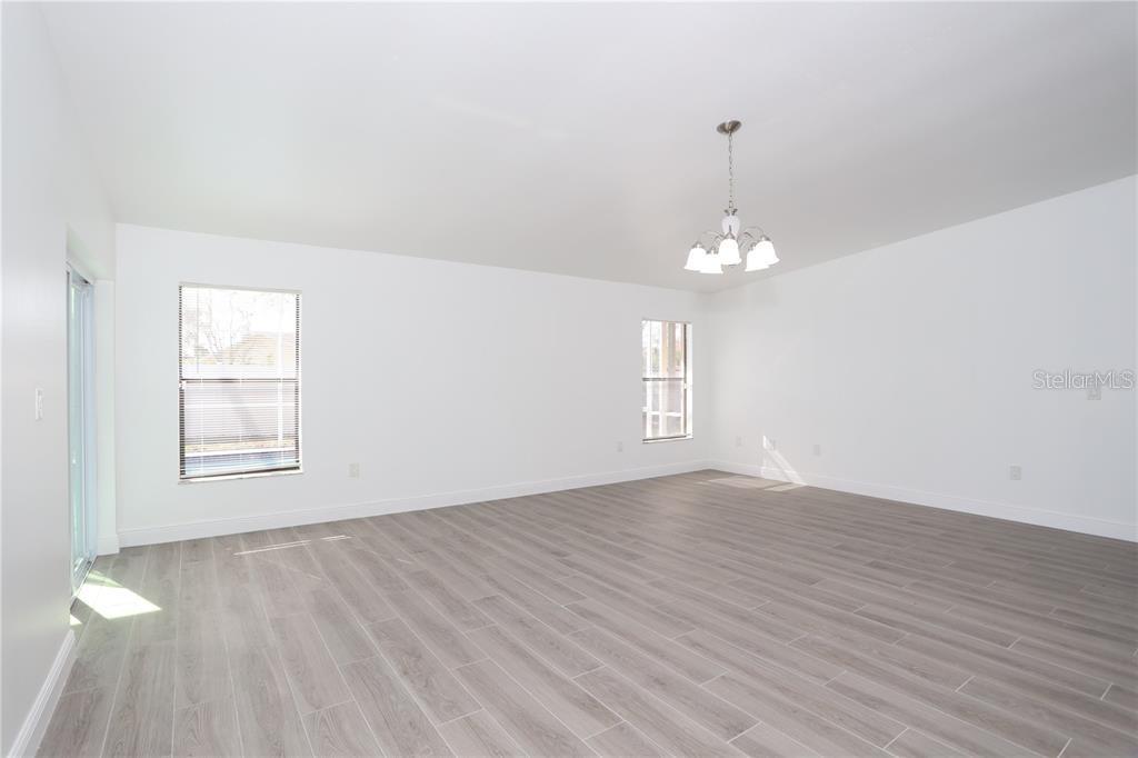 An empty room with white walls, light wood-look flooring, two windows, and a chandelier — 620 HERALDO COURT, KISSIMMEE, FL