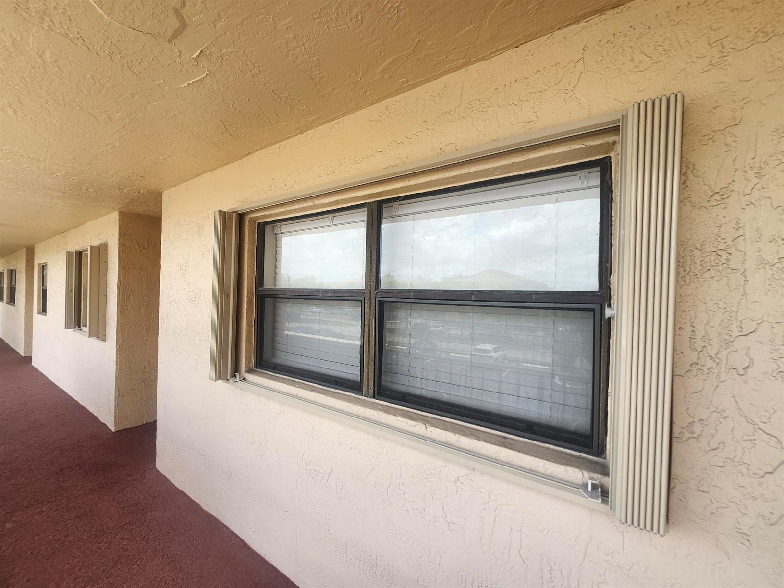 A beige exterior wall features a window with vertical accordion-style hurricane shutters — 3470 Foxcroft Road # 207, Miramar FL 33025, MIRAMAR, FL