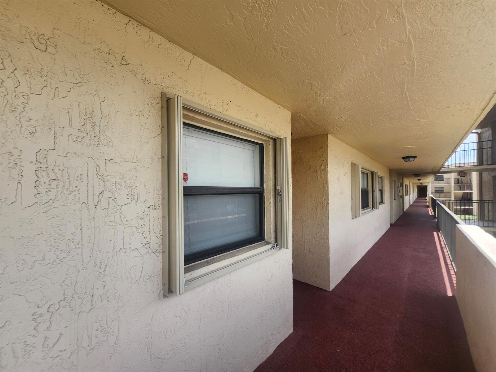 An exterior view of an apartment building hallway with textured walls and windows — 3470 Foxcroft Road # 207, Miramar FL 33025, MIRAMAR, FL