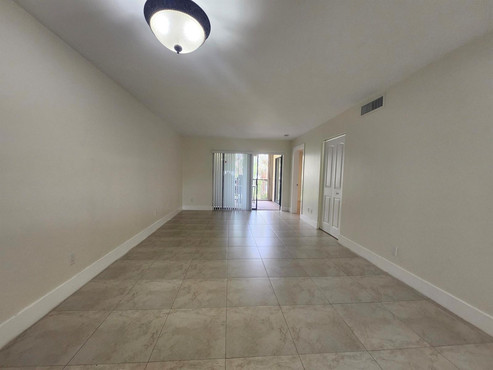 An empty room with beige tile flooring, white walls, a ceiling light, and a sliding door — 3470 Foxcroft Road # 207, Miramar FL 33025, MIRAMAR, FL