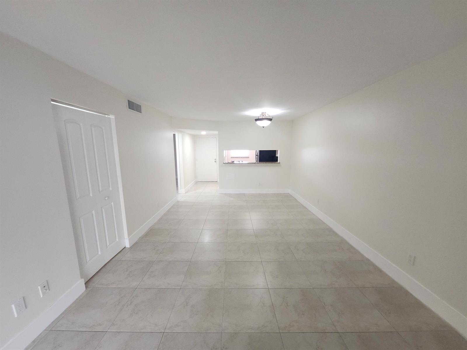 An empty room with light-colored tile flooring, white walls, and a kitchen pass-through window — 3470 Foxcroft Road # 207, Miramar FL 33025, MIRAMAR, FL