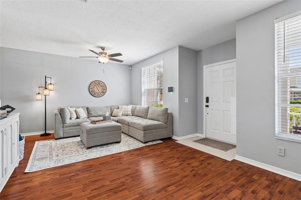 A living room features light gray walls, wood-look flooring, a sectional sofa, and a ceiling fan — 3541 RED ROCK DRIVE, LAND O LAKES, FL