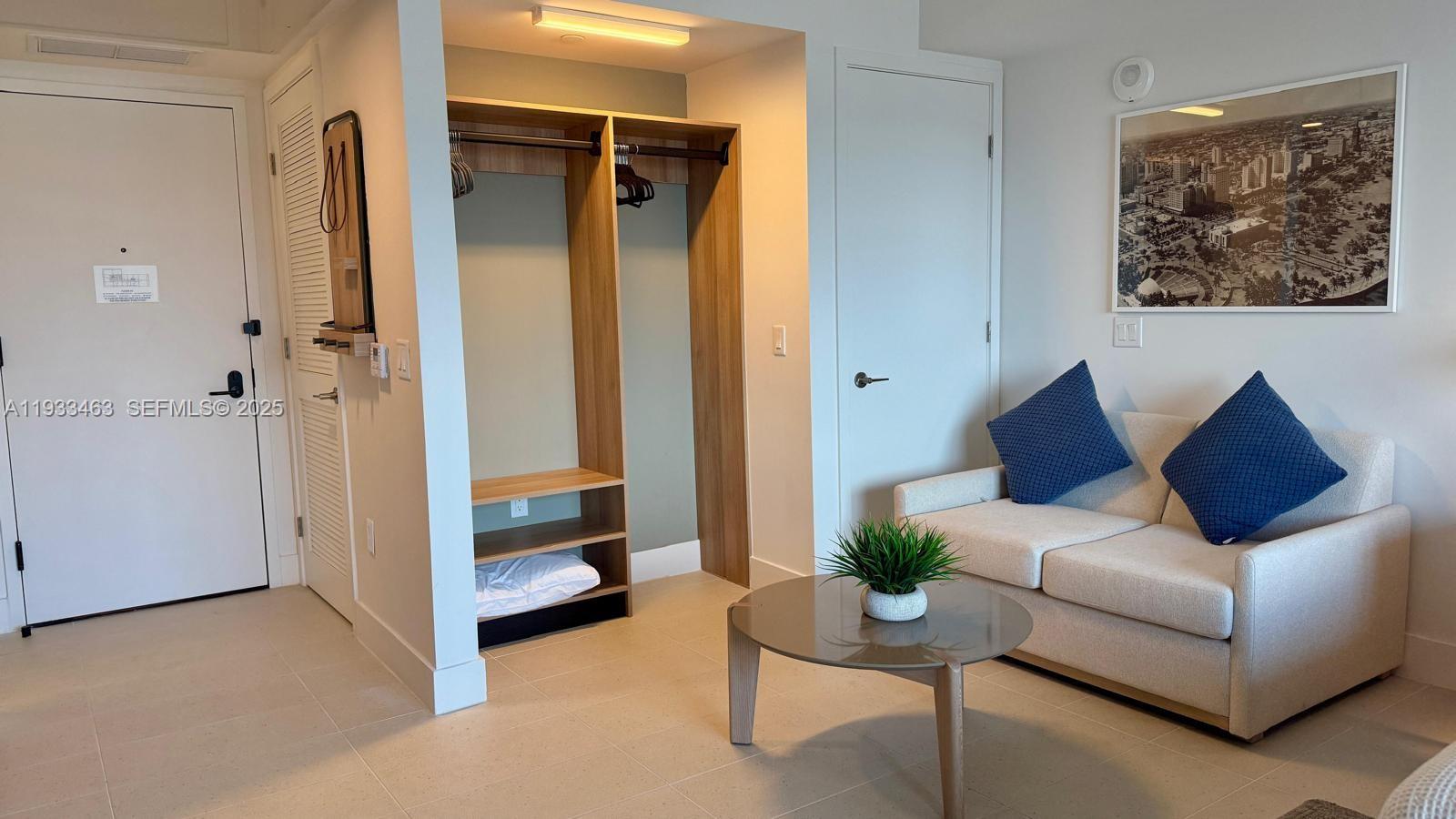 A room features a beige sofa, a round coffee table, and an open wooden closet — 159 NE 6th St # 4010, Miami FL 33132, MIAMI, FL